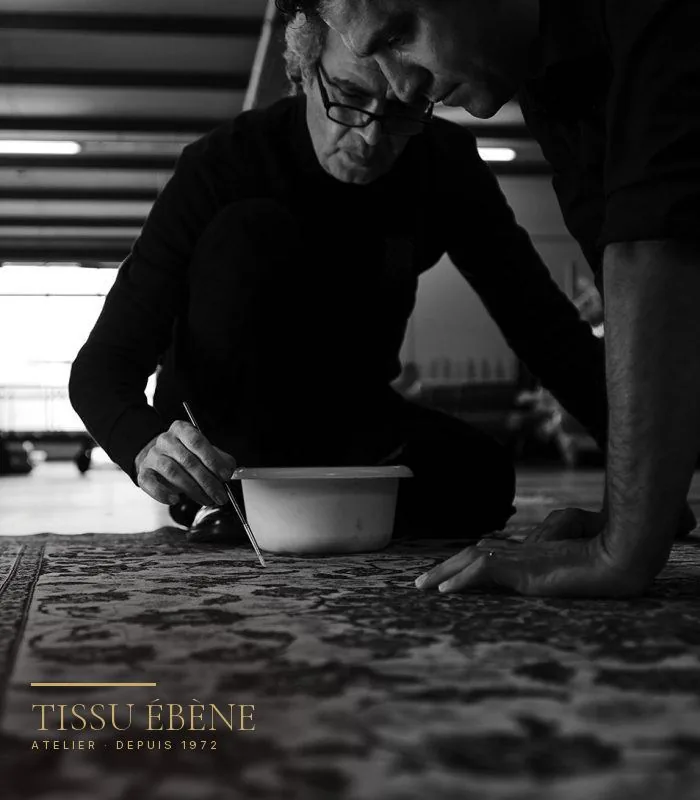 Artisan de Tissu Ébène traitant une zone précise d’un tapis à l’atelier