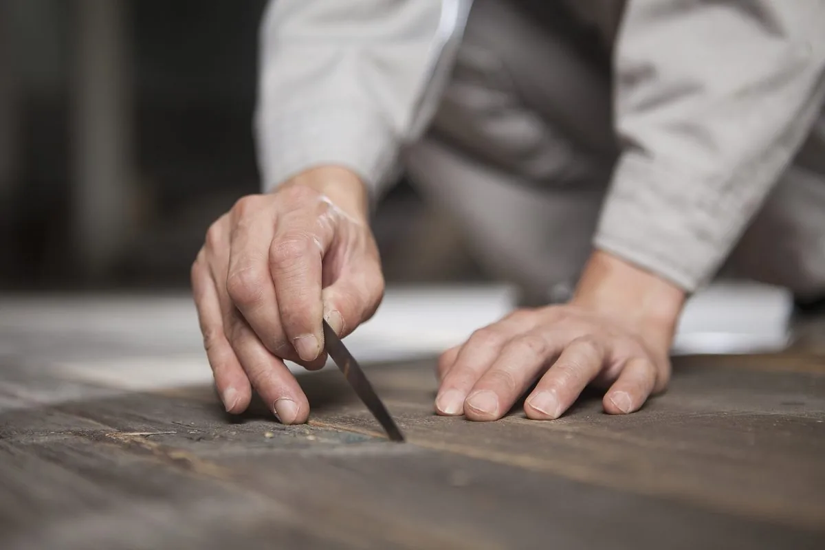 Mains d’artisan guidant un ciseau à bois sur un plateau de bois sombre, gros plan à l’atelier