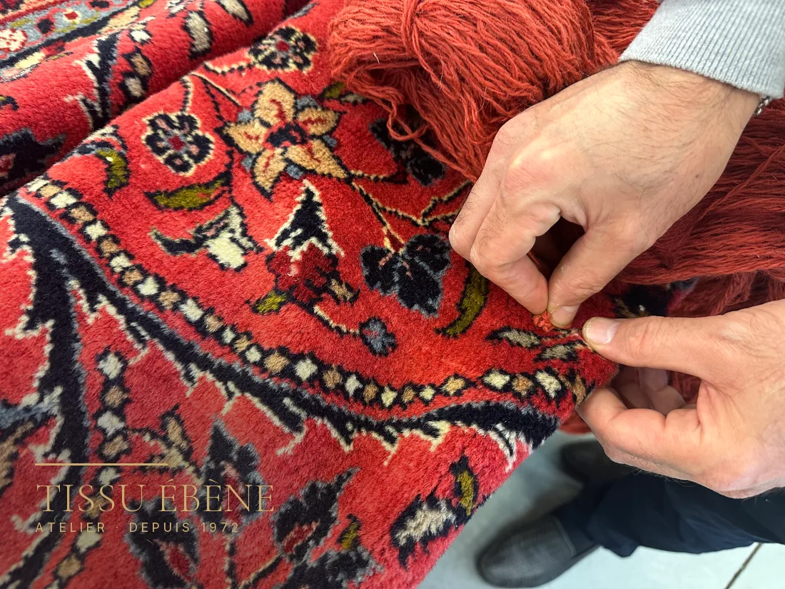 Expert écartant le velours d’un tapis persan pour observer le nœud à la base des brins