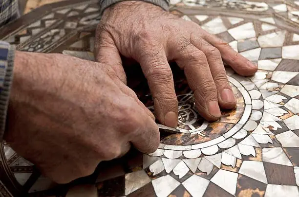 Mains d’artisan incrustant des éclats de nacre dans un plateau marqueté