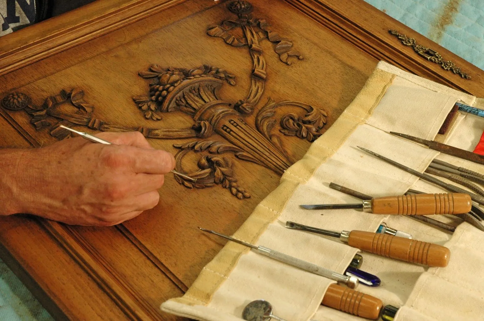 Main guidant un outil fin sur un panneau de bois sculpté, trousse de gouges et ciseaux déroulée