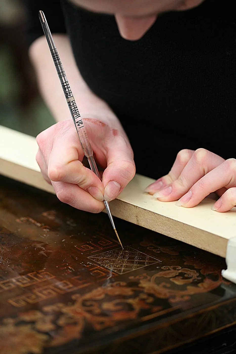 Restauratrice de l’atelier Tissu Ébène retouchant au pinceau fin un décor laqué japonais — restauration de meubles japonais à Paris
